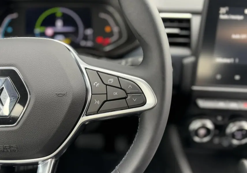 Gros plan sur le volant noir de la Renault Arkana 2024, avec commandes intégrées et tableau de bord numérique flou en arrière-plan.