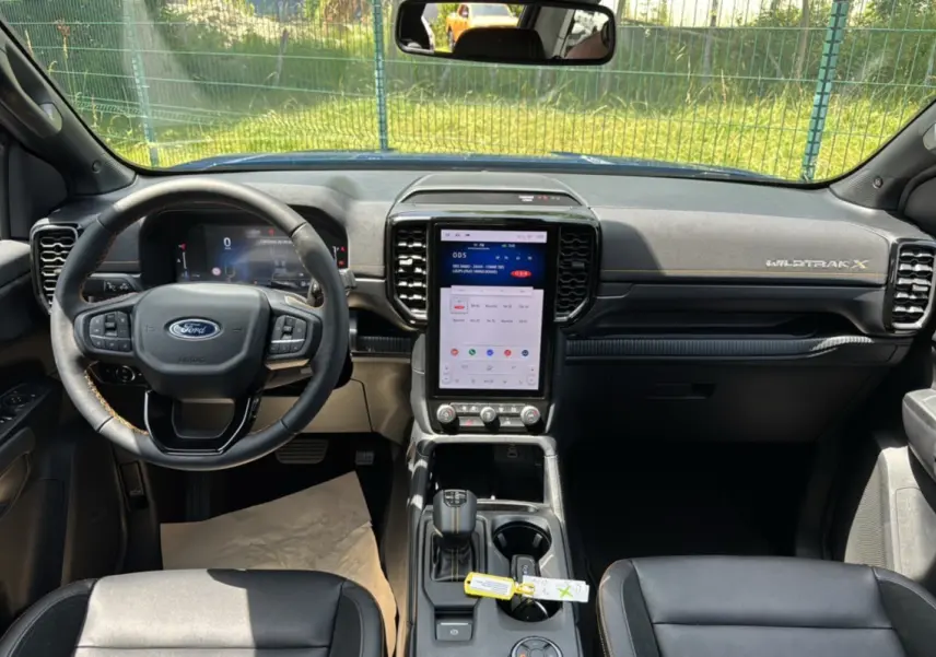 Vue intérieure avant du Ford Ranger Wildtrak X 2026, tableau de bord noir avec écran tactile vertical et volant cuir multifonctions.