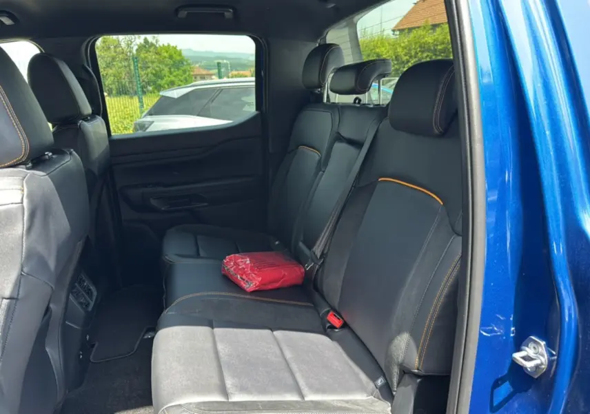 Vue intérieure arrière côté droit du Ford Ranger 205 Wildtrak X bleu lightning avec sièges noirs et surpiqûres orange.