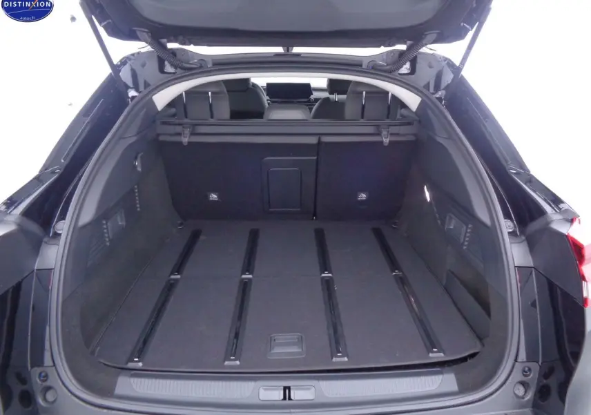 Coffre ouvert d'une Citroën C5 X noire métal, vue arrière montrant l'espace de chargement plat et les sièges rabattus.