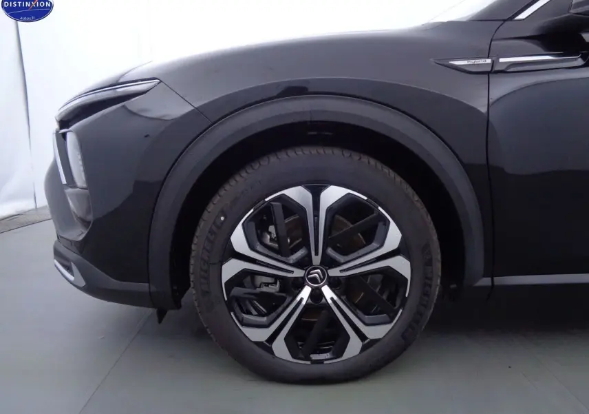 Gros plan sur la roue avant gauche noire métal du Citroën C5 X hybride avec logo et badge Hybrid sur l'aile.