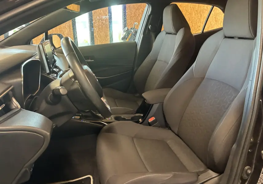 Intérieur avant de la Toyota Corolla 1.8 122 Dynamic 2020, sièges tissu noirs et volant multifonctions visible côté conducteur.