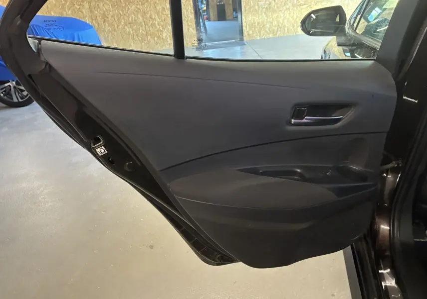 Porte arrière côté gauche ouverte d'une Toyota Corolla noire, montrant le panneau intérieur en tissu noir avec poignée et commandes fenêtres.