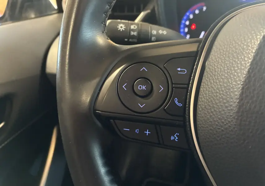 Gros plan sur les commandes gauche du volant cuir alu de la Toyota Corolla 1.8 122 Dynamic noire de 2020.