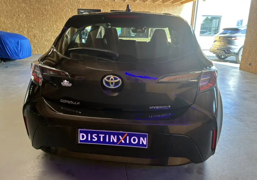 Vue arrière d'une Toyota Corolla noire hybride 2020 avec logo Toyota et plaques Distinxion visibles en intérieur garage.