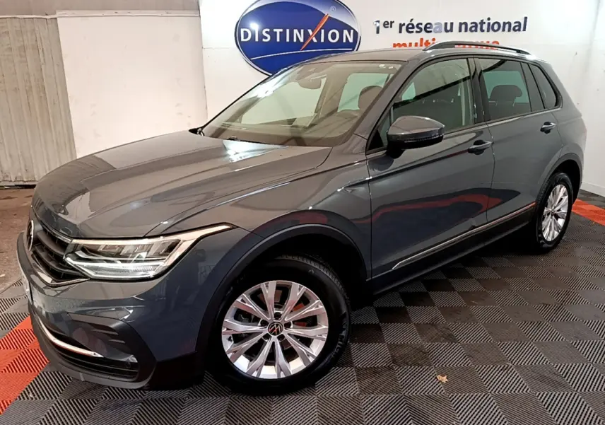 Volkswagen Tiguan gris clair en 3/4 avant droit, avec jantes alliage et feux LED allumés.