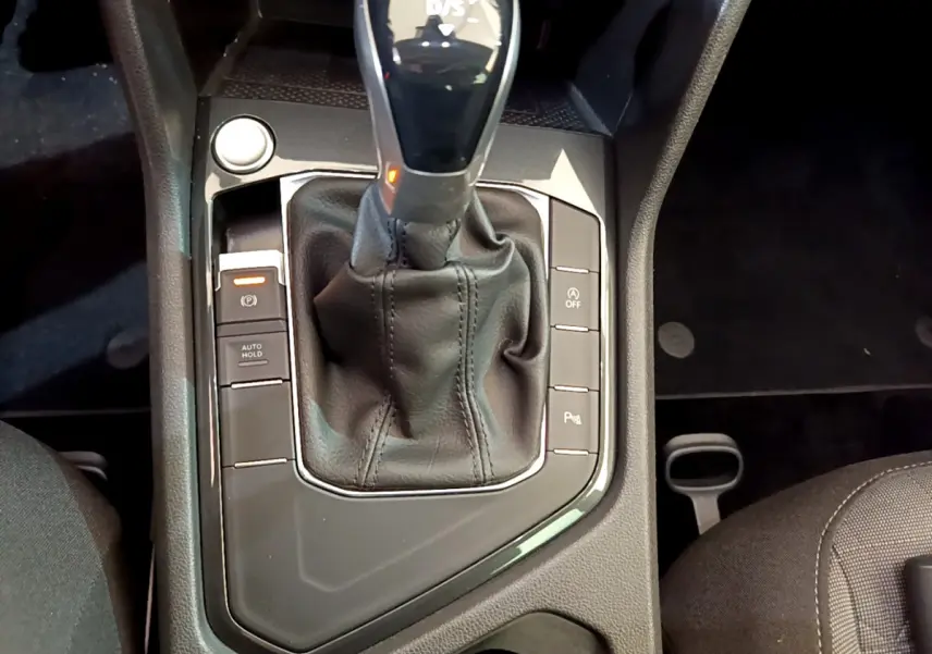 Gros plan sur la console centrale du Volkswagen Tiguan gris clair, mettant en valeur le levier de vitesse automatique et les boutons de contrôle.