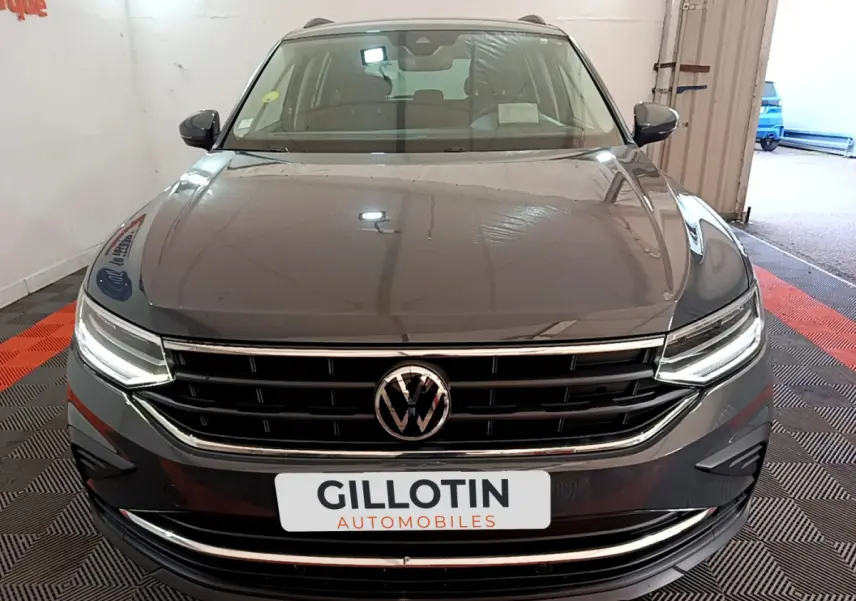 Vue avant d'un Volkswagen Tiguan gris clair 2021 avec phares LED allumés et calandre chromée dans un garage.