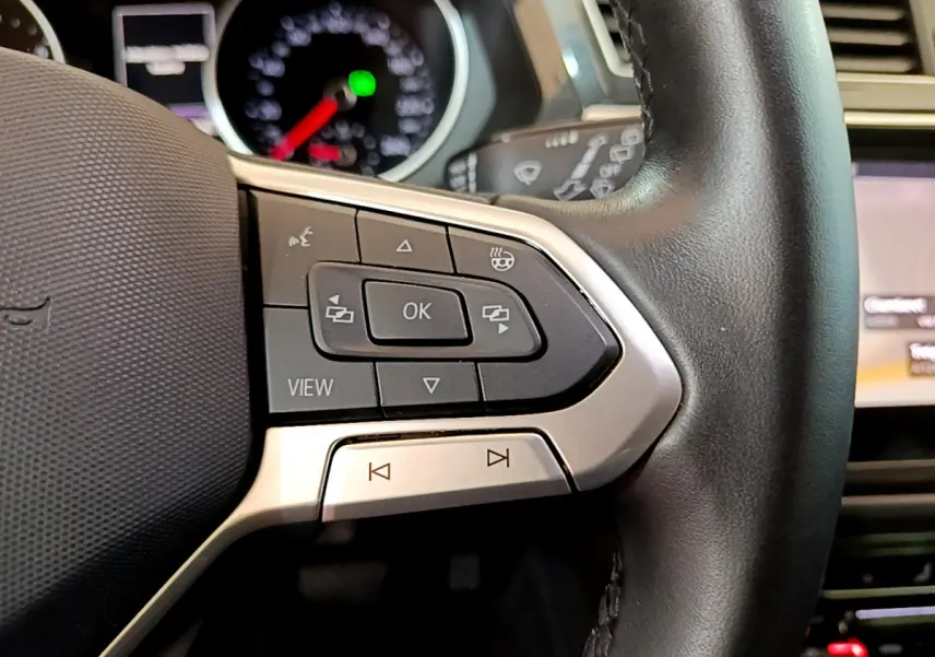 Gros plan sur les commandes gauche du volant cuir noir du Volkswagen Tiguan 2021, avec tableau de bord flou en arrière-plan.