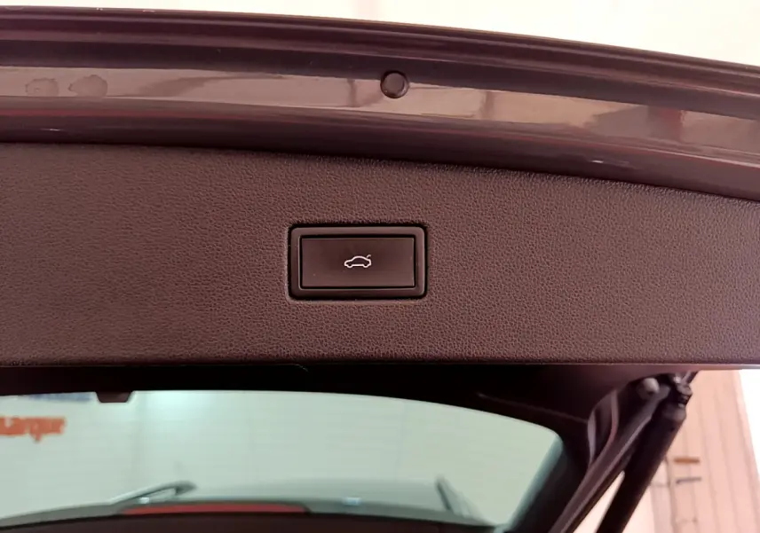 Gros plan sur le bouton d’ouverture électrique du coffre du Volkswagen Tiguan gris clair, vue depuis l’arrière ouvert.
