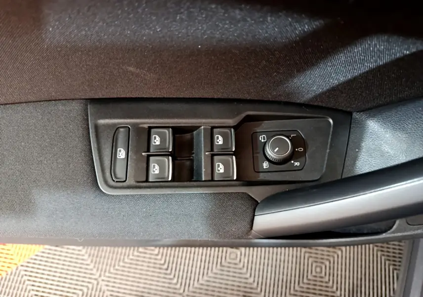 Gros plan sur les commandes de lève-vitres et réglage des rétroviseurs côté conducteur du Volkswagen Tiguan gris clair.