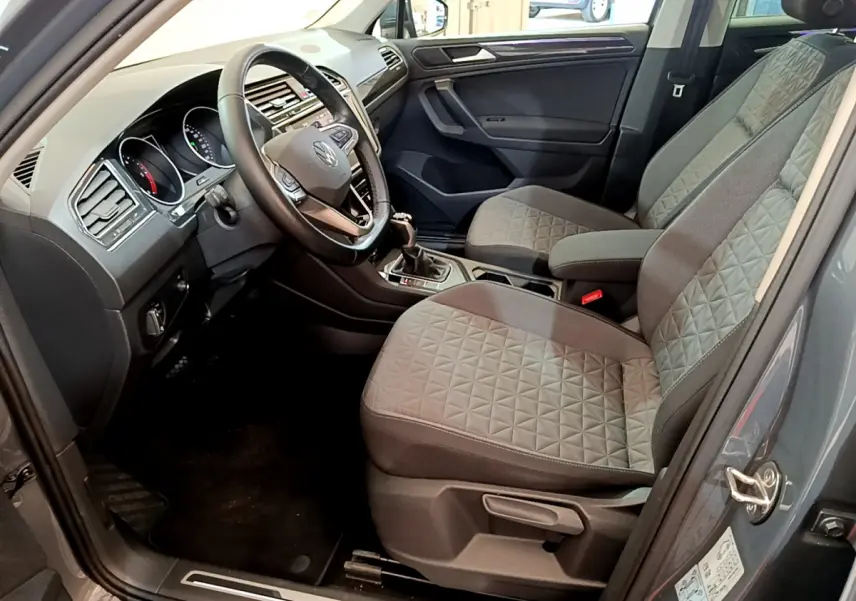 Vue intérieure côté conducteur du Volkswagen Tiguan gris clair 2021 avec sièges tissu gris et volant cuir multifonctions.