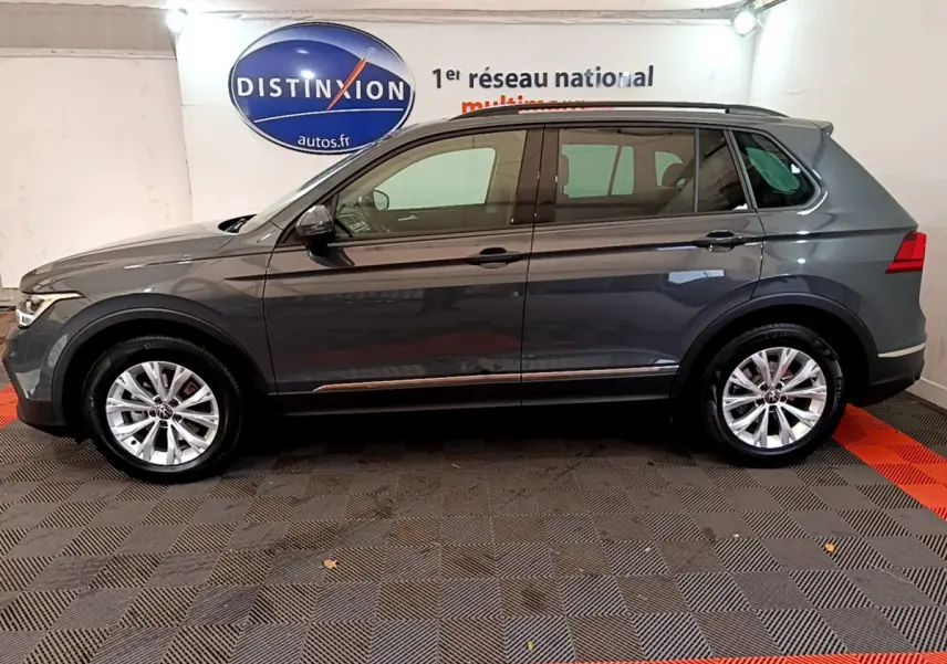 Vue de profil côté gauche d’un Volkswagen Tiguan gris clair 2021 dans un showroom avec sol à damier noir et rouge.