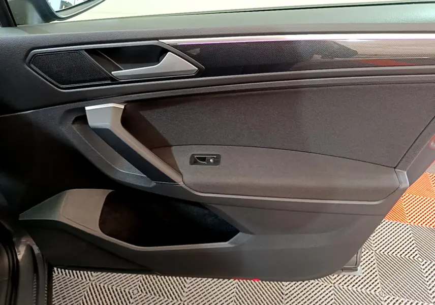 Vue rapprochée de la porte intérieure côté droit du Volkswagen Tiguan gris clair, avec poignée argentée et garniture noire.