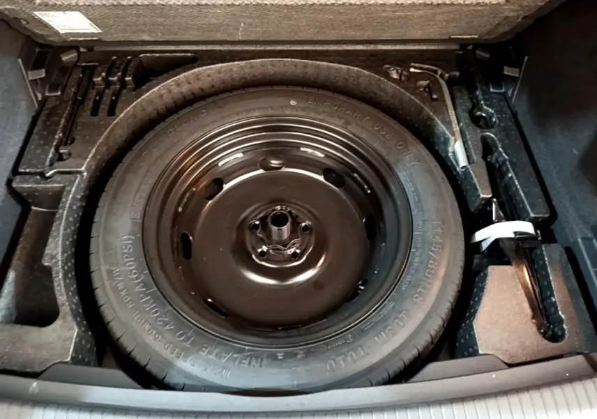 Gros plan sur la roue de secours noire dans le coffre du Volkswagen Tiguan gris clair, avec outils de changement visibles.