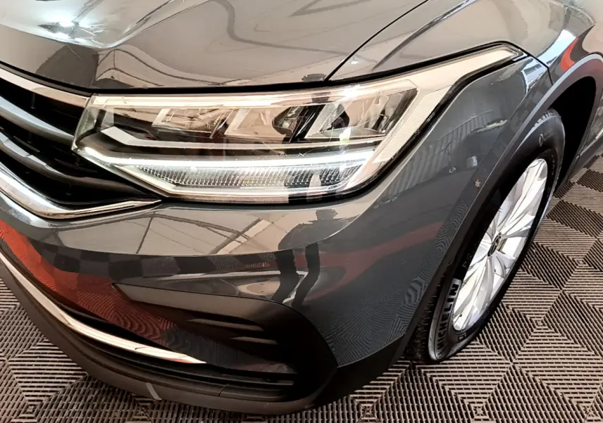 Gros plan sur l'avant droit gris clair du Volkswagen Tiguan 2.0 TDI 150 DSG7 avec phare LED et jante alliage visible.