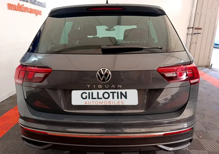 Vue arrière d'un Volkswagen Tiguan gris clair 2021 avec feux LED et logo VW bien visibles en intérieur showroom.