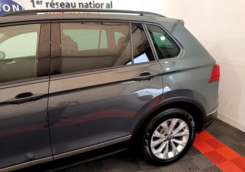 Vue latérale côté droit du Volkswagen Tiguan gris clair, mettant en valeur la roue arrière et les vitres teintées.