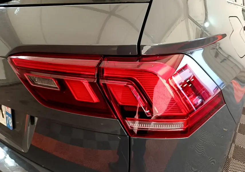 Gros plan sur le feu arrière droit rouge d’un Volkswagen Tiguan gris clair, avec reflet sur la carrosserie lisse.