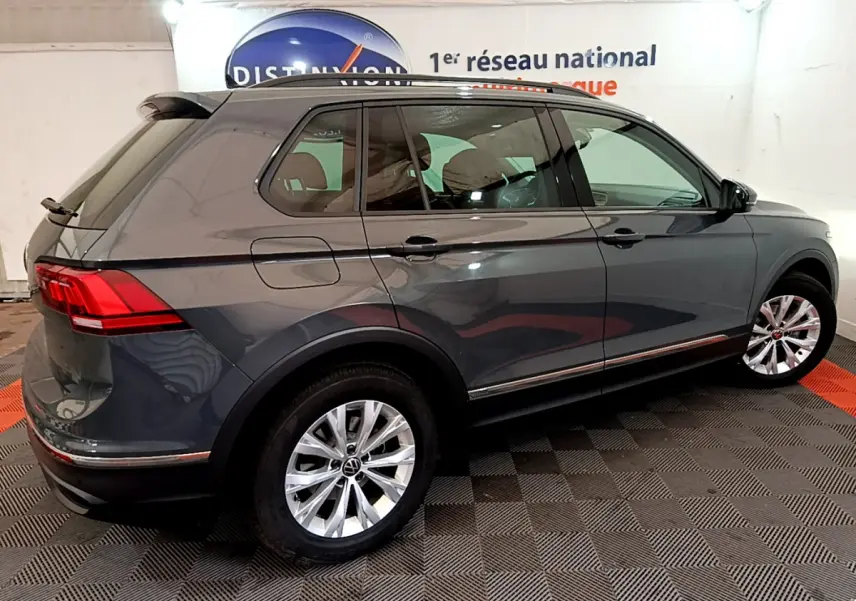 Vue 3/4 arrière droite d'un Volkswagen Tiguan gris clair garé en intérieur avec jantes argentées et vitres teintées.