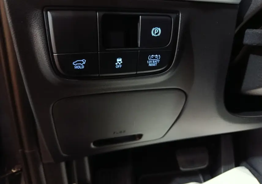 Détail intérieur côté conducteur du Hyundai Tucson gris clair 2025 montrant les boutons de frein à main électrique et assistance stabilité.
