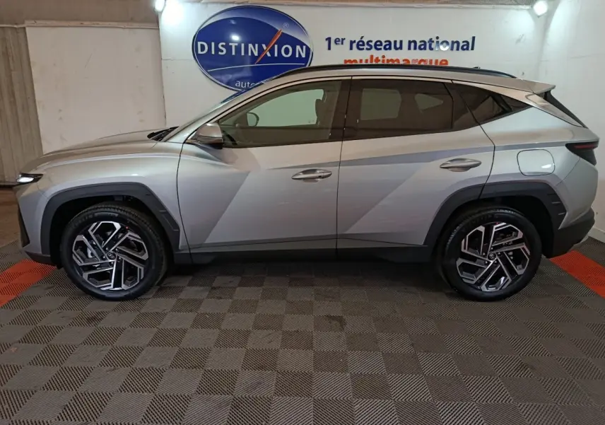 Vue de profil côté gauche d'un Hyundai Tucson 1.6 Hybrid gris clair 2025, avec jantes alliage et toit noir.