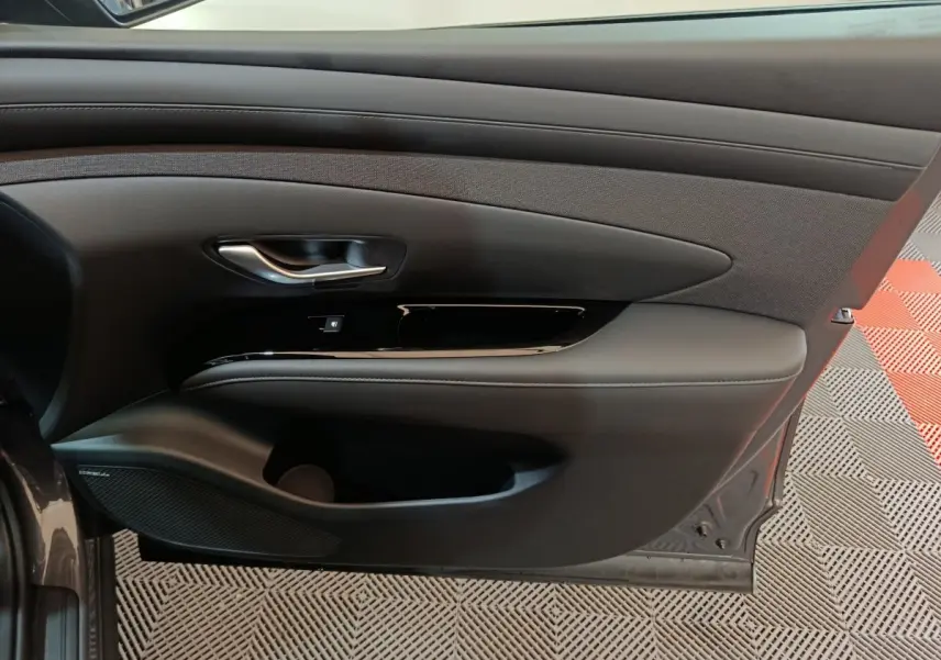 Vue intérieure côté gauche de la porte avant d'un Hyundai Tucson gris clair, avec habillage noir et insert tissu.