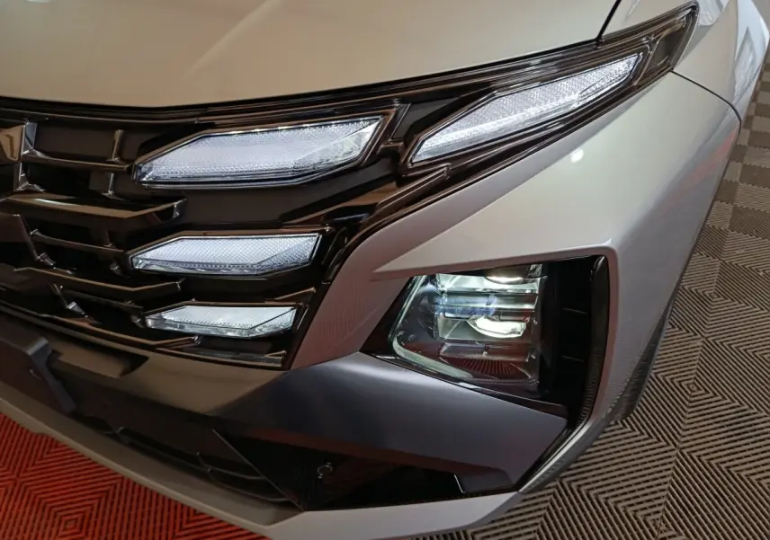 Gros plan sur le phare avant droit et la calandre noire du Hyundai Tucson gris clair 2025 hybride.