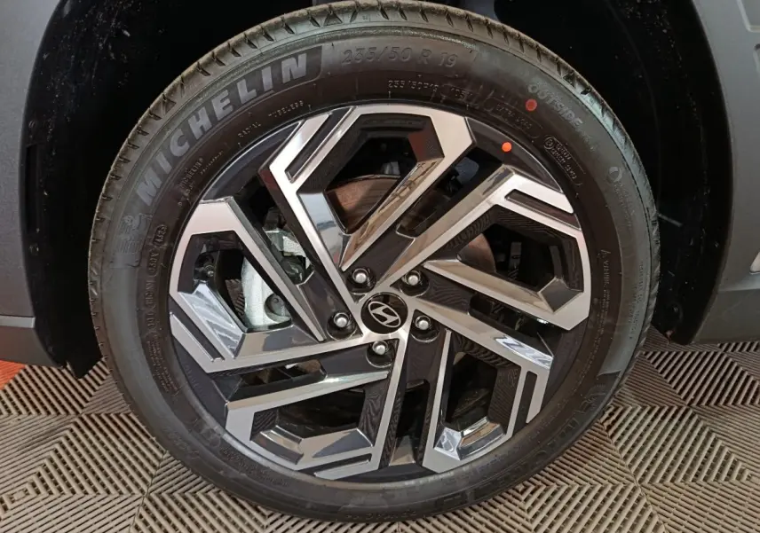 Gros plan sur la roue avant droite du Hyundai Tucson 2025 gris clair, mettant en valeur la jante alliage au design géométrique.