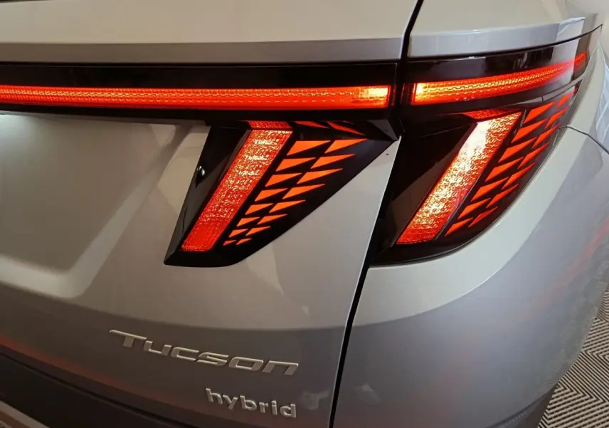 Gros plan sur le feu arrière droit rouge allumé d’un Hyundai Tucson hybride gris clair avec logo et inscription hybrid visibles.