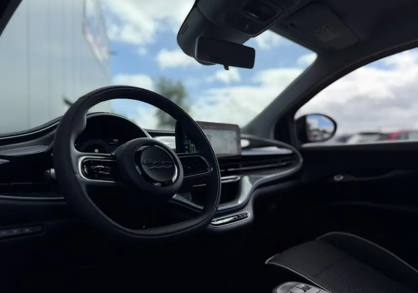 Intérieur de la Fiat 500 électrique 2024 vu côté conducteur, volant noir Soft-Touch et écran tactile central.