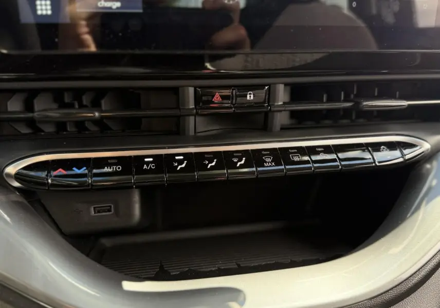 Gros plan sur la console centrale noire de la Fiat 500 électrique 2024, montrant les commandes de climatisation et un port USB.