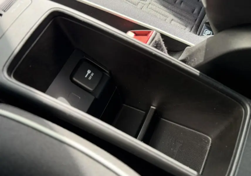 Vue rapprochée de la console centrale noire avec prise 12V et espace de rangement dans la Fiat 500 électrique blanche.