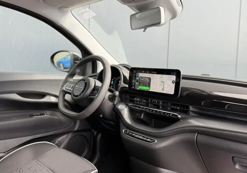 Vue intérieure côté conducteur de la FIAT 500 électrique 2024, tableau de bord noir avec écran tactile central et volant Soft-Touch.