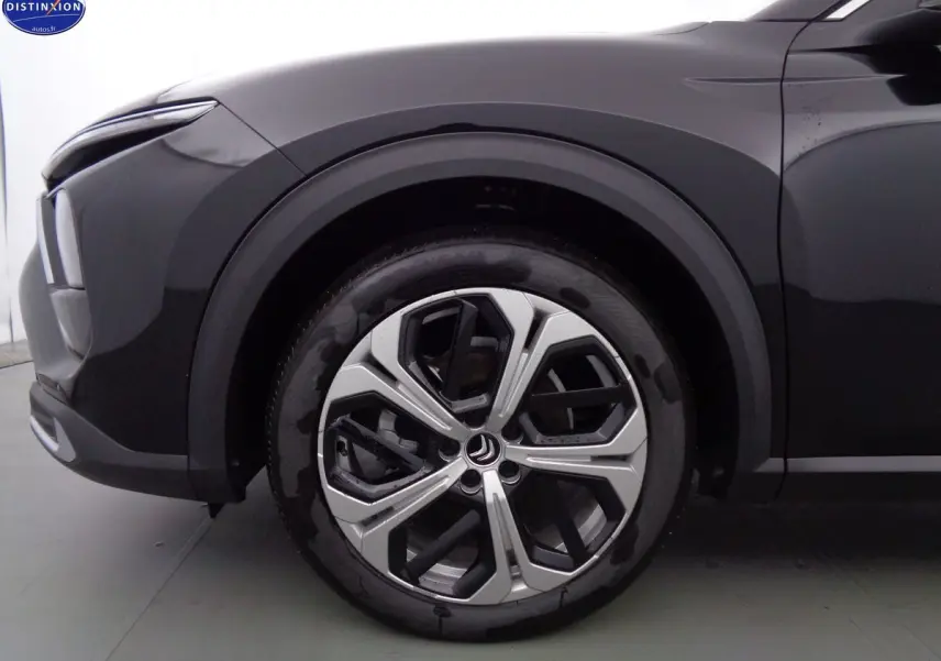 Gros plan sur la roue avant gauche de la Citroën C5 X noire métal, mettant en valeur la jante bi-ton au design moderne.