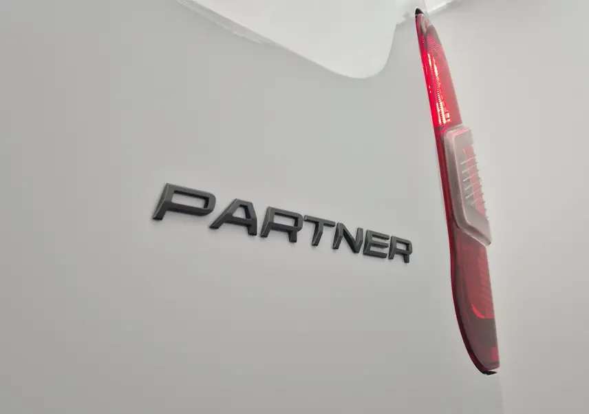 Gros plan sur l'arrière blanc du Peugeot Partner avec le logo "PARTNER" et le feu arrière droit allumé.