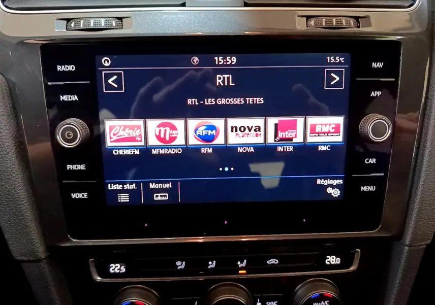 Vue rapprochée de l’écran tactile central de la Volkswagen Golf noire, affichant les stations radio et commandes climatisation.