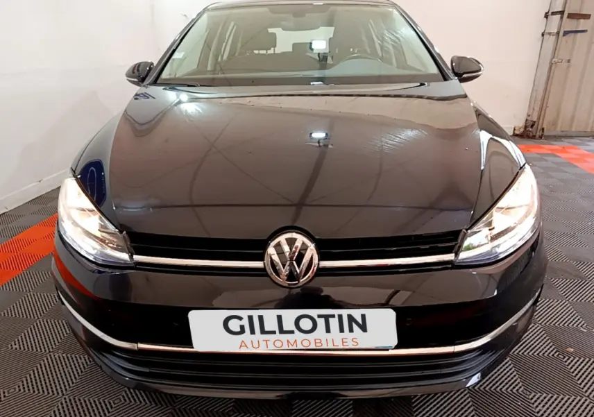 Vue avant d'une Volkswagen Golf noire 2018 avec phares allumés dans un garage intérieur.