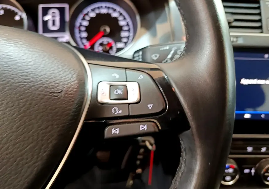 Gros plan sur le volant cuir côté gauche de la Volkswagen Golf noire, avec commandes multifonctions et tableau de bord en arrière-plan.