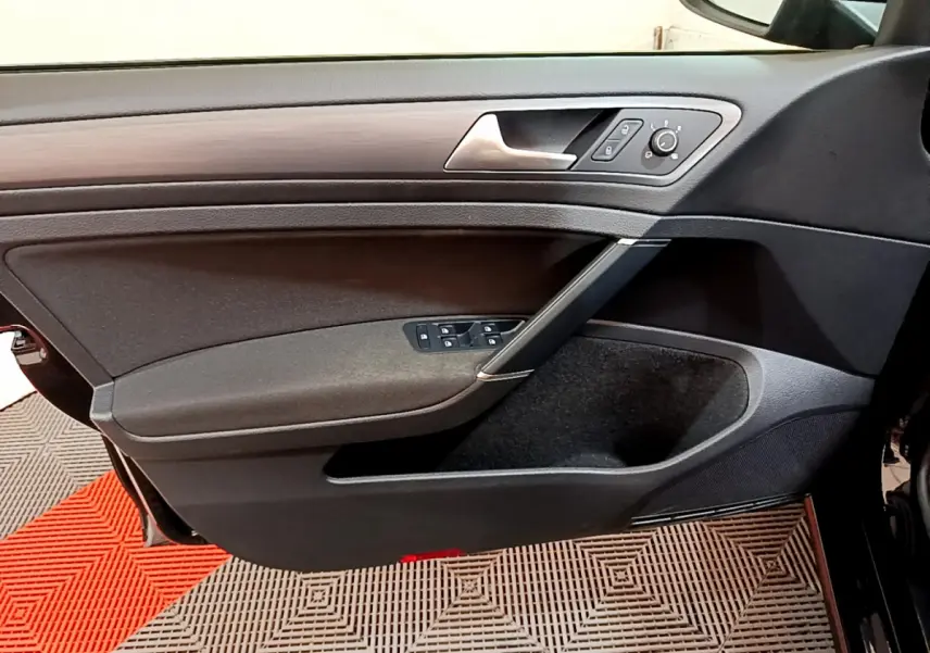 Vue rapprochée de la porte avant gauche noire de la Volkswagen Golf 2018 avec commandes électriques et insert décor bois.