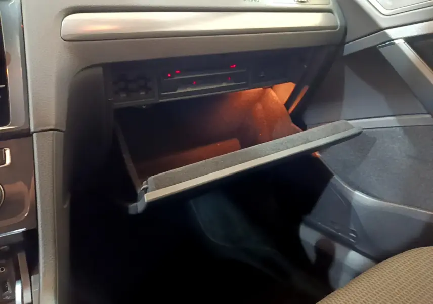 Vue intérieure du coffre à gants ouvert côté passager d'une Volkswagen Golf noire, éclairage intérieur orange visible.