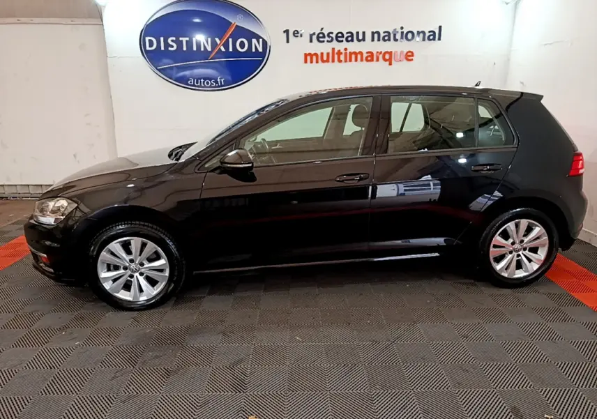 Profil côté gauche d’une Volkswagen Golf noire 2018, finition Confort Business, sur sol damier en intérieur showroom.