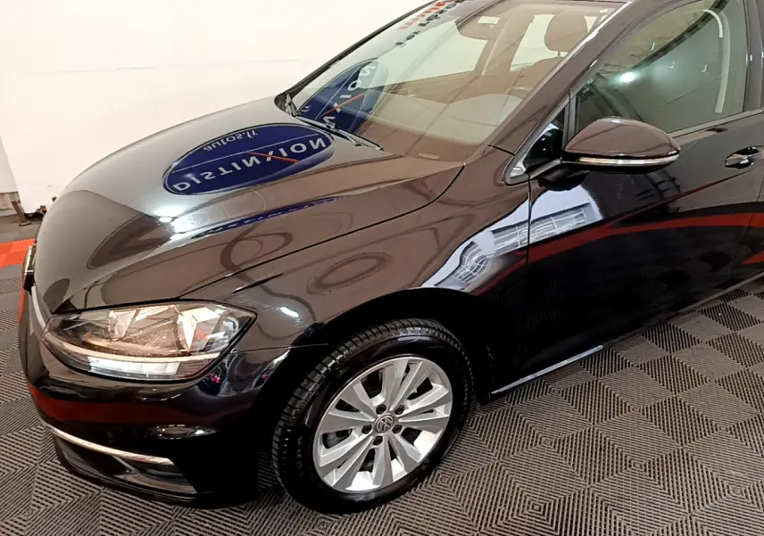 Vue 3/4 avant droit d'une Volkswagen Golf noire brillante avec jantes alliage et phares allumés.