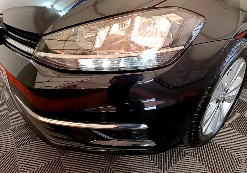 Gros plan sur l'avant droit noir d'une Volkswagen Golf 2018, mettant en valeur le phare allumé et la jante alliage.