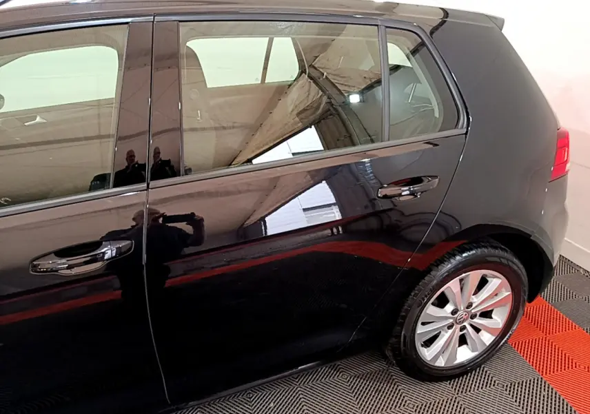 Vue latérale droite d'une Volkswagen Golf noire, mettant en valeur les portes arrière et la roue arrière avec jante argentée.