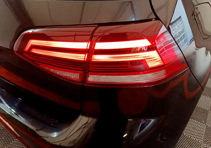 Gros plan sur le feu arrière droit allumé d'une Volkswagen Golf noire, reflétant l'environnement intérieur.