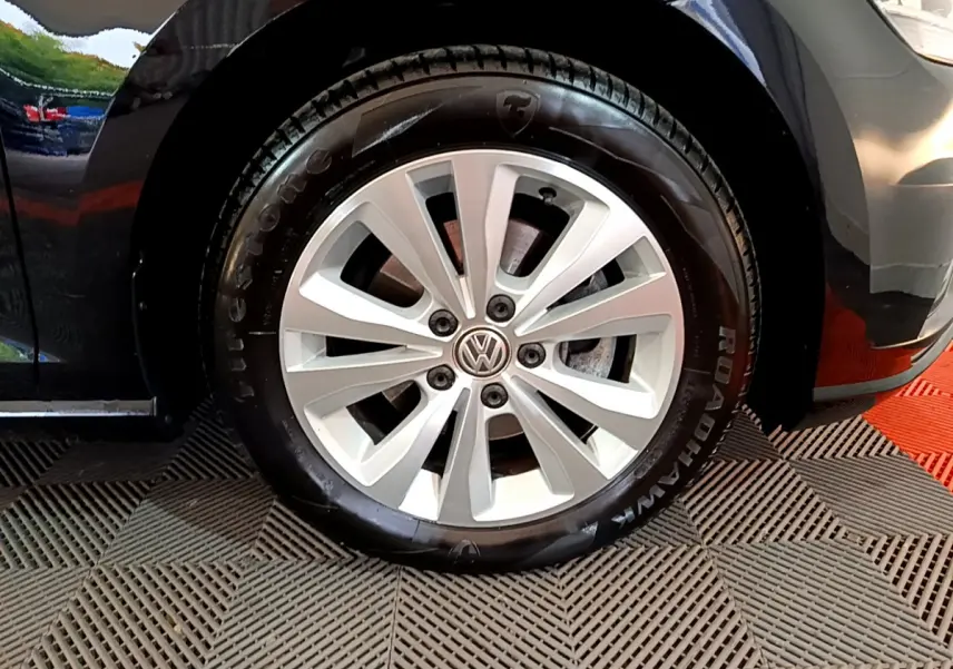 Gros plan sur la roue avant droite d'une Volkswagen Golf noire, avec jante argentée et logo VW central.