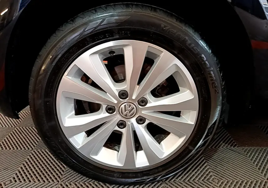 Gros plan sur la roue avant droite de la Volkswagen Golf noire, jante alliage argentée avec logo VW au centre.