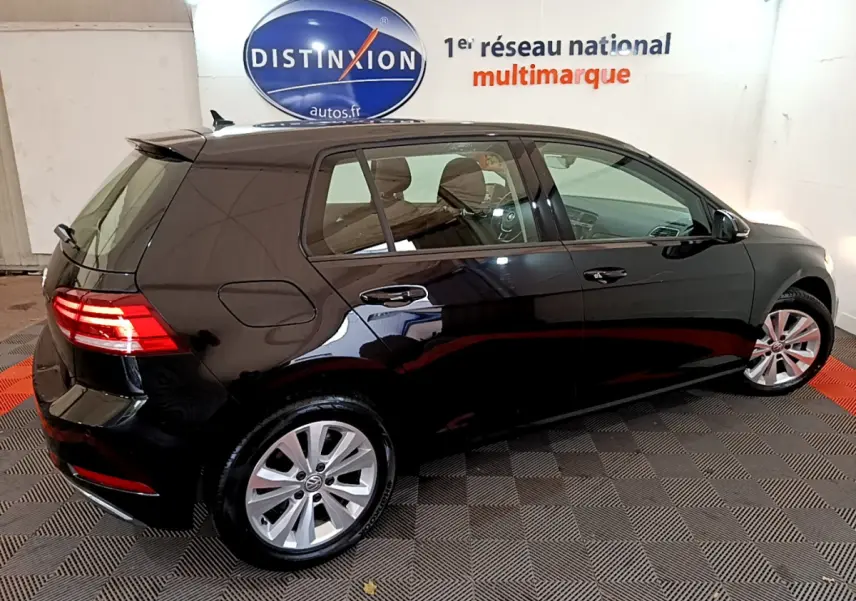 Vue 3/4 arrière droite d'une Volkswagen Golf noire 2018 avec feux arrière allumés dans un showroom.