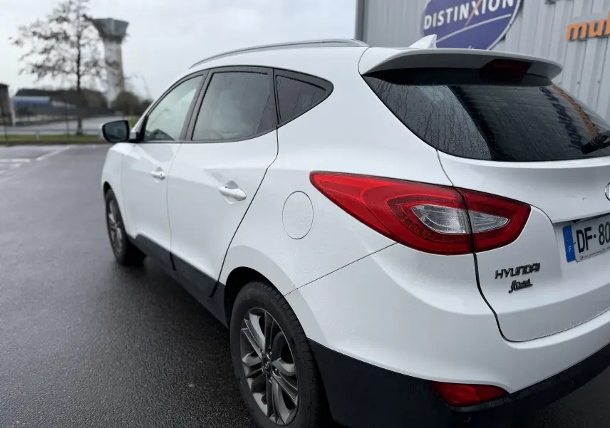 Vue 3/4 arrière droite d'un Hyundai ix35 blanc 2014 avec feux arrière rouges et jantes alliage foncé.